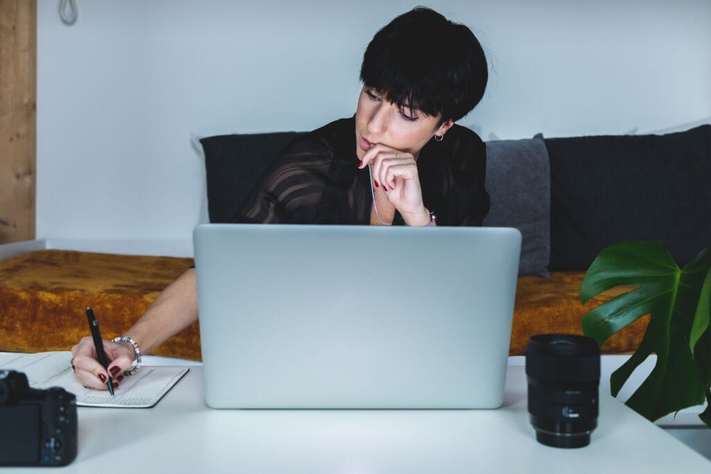 woman-at-laptop-in-thought-as-she-writes-in-a-notebook