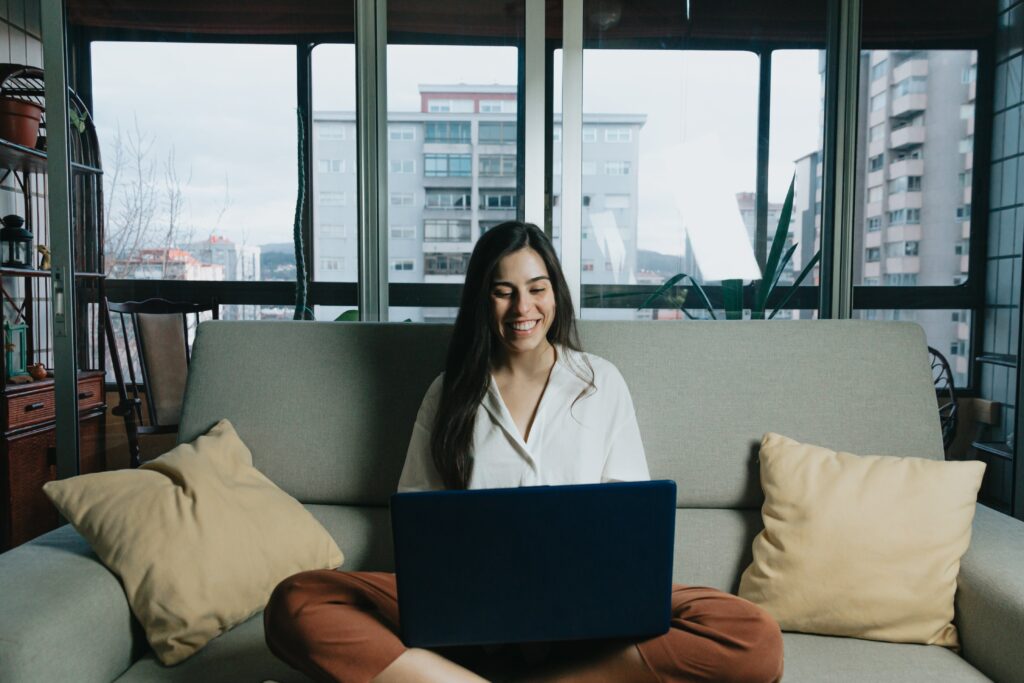 woman-sits-on-a-couch-while-looking-at-laptop